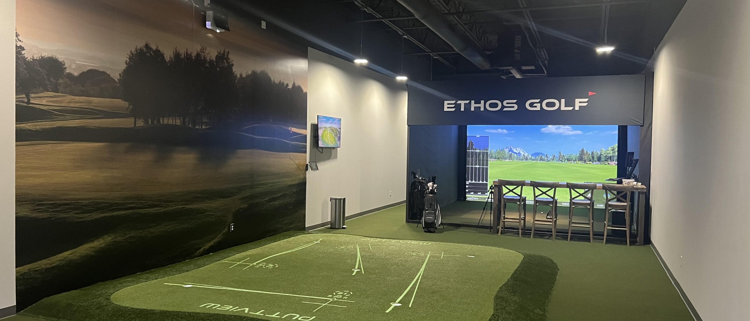 A modern indoor golf facility in Allen, Texas, featuring a putting green and a large golf simulator screen. The area is branded with 