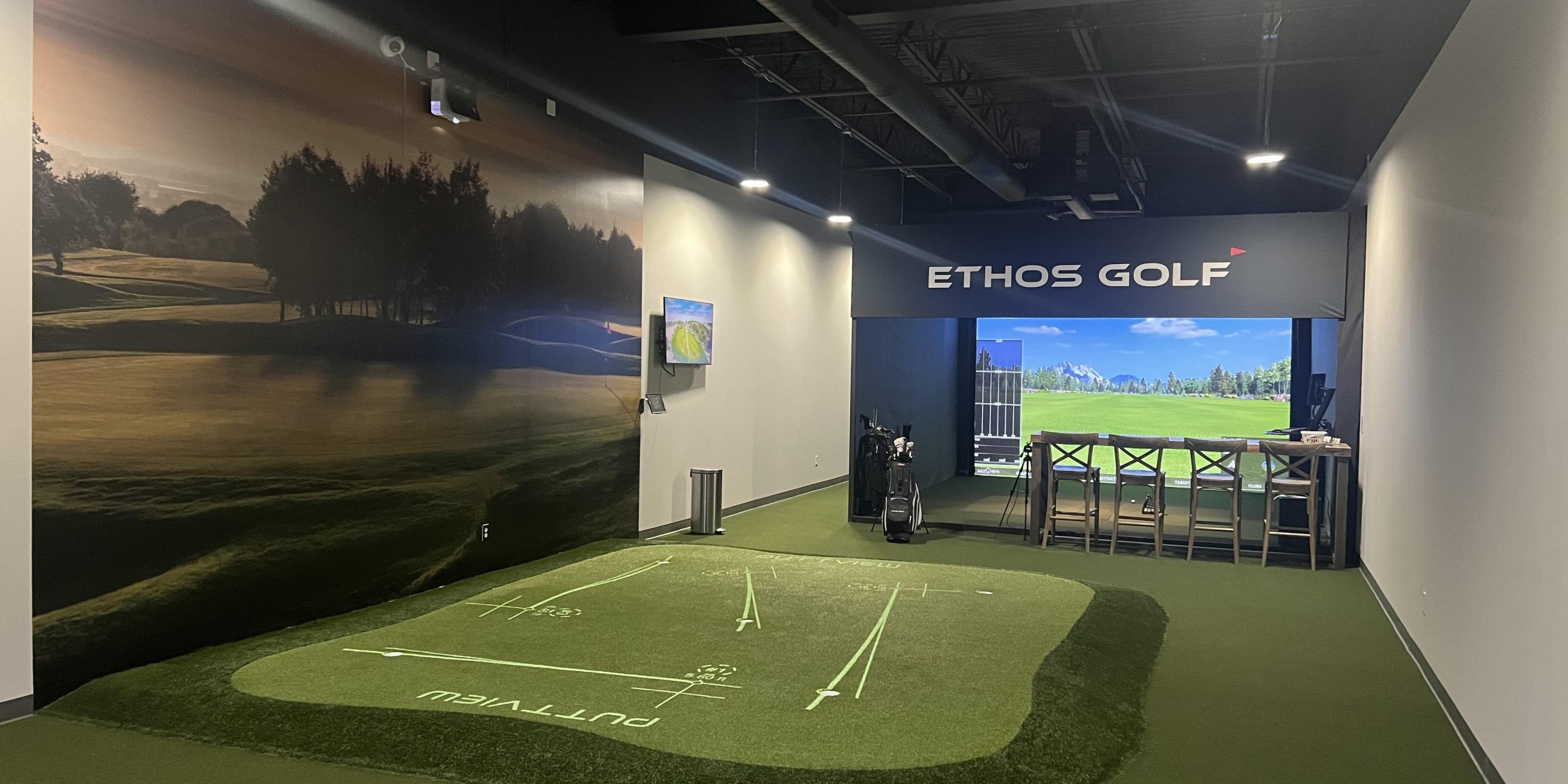 A modern indoor golf facility in Allen, Texas, featuring a putting green and a large golf simulator screen. The area is branded with 